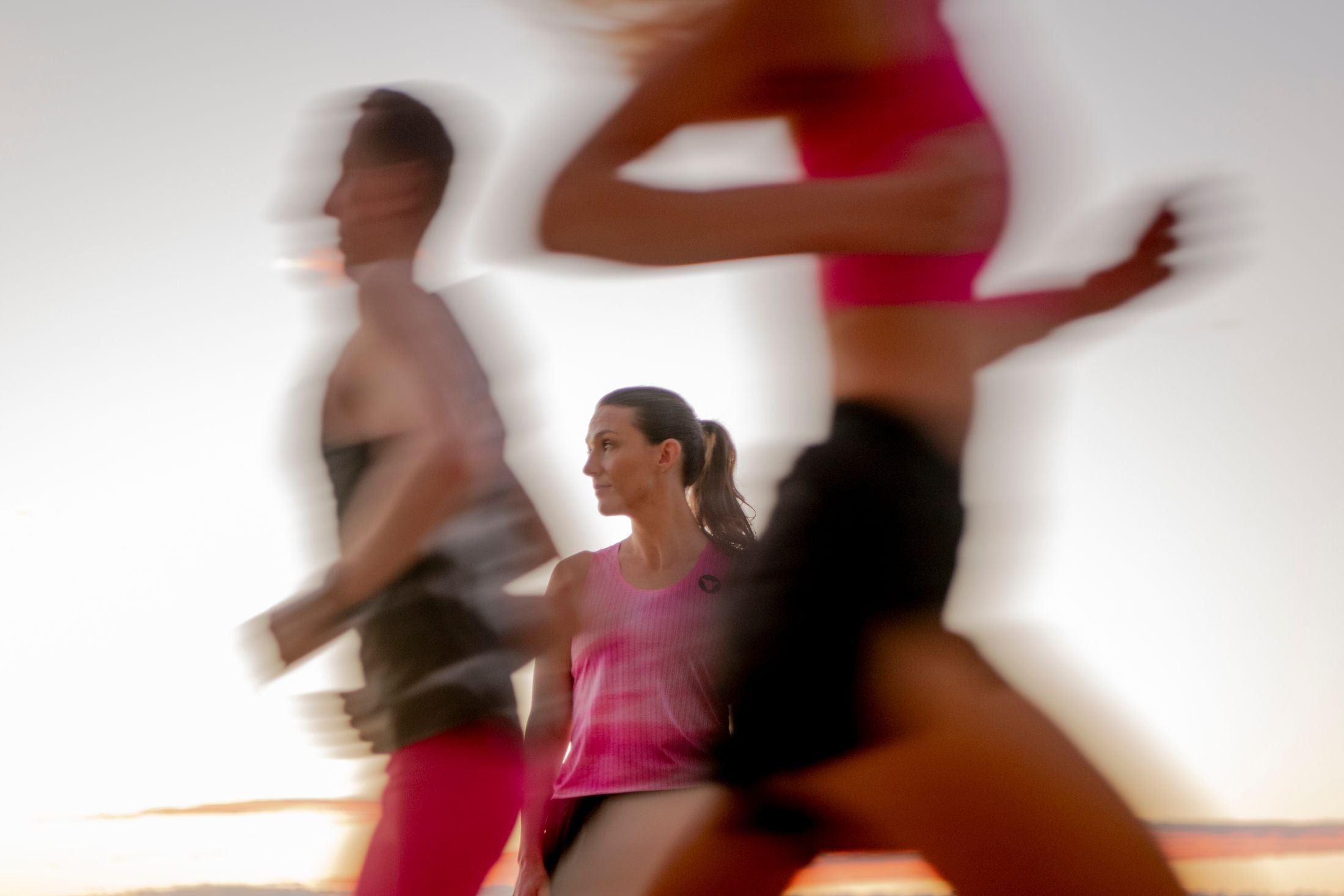 A runner stands still in focus while training partners blur past at sunrise