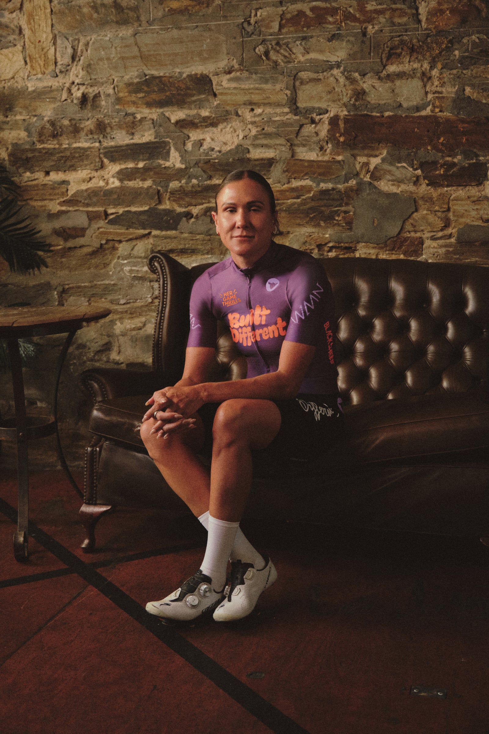 Carlee Taylor seated on a leather sofa in a purple cycling jersey